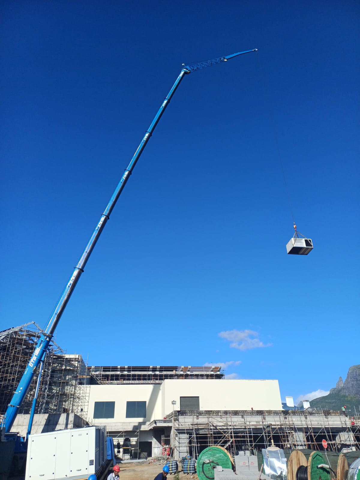 Blue crane lifting an AC unit to a roof