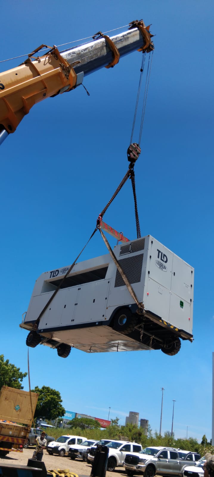 Crane lifting a TLD ground power unit against a blue sky